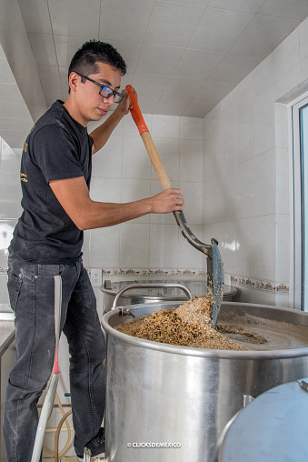 man moving a pot of boiling water with barley with a shovel for craft beer production
