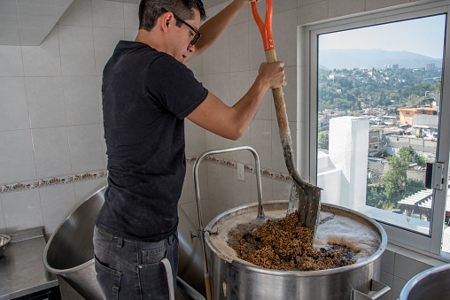 Latino man shoveling an industrial pot with barley for craft beer production