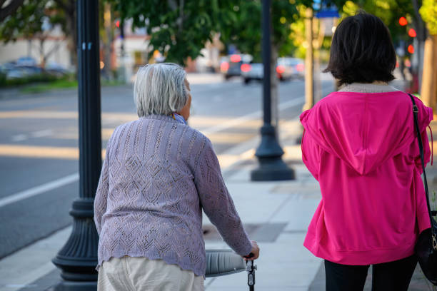 istock Senior woman walking using a mobility walker on the pedestrian footpath, accompanied by her daughter. 1928805174