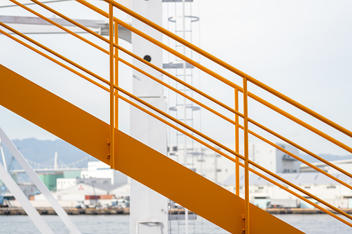 Side view at the yellow metal railing banister or handrail of the metal stairway with background of industrial working place.