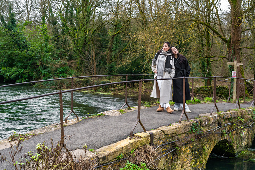 Two women are traveling together and taking photos on a bridge across river in Cotswold district, UK