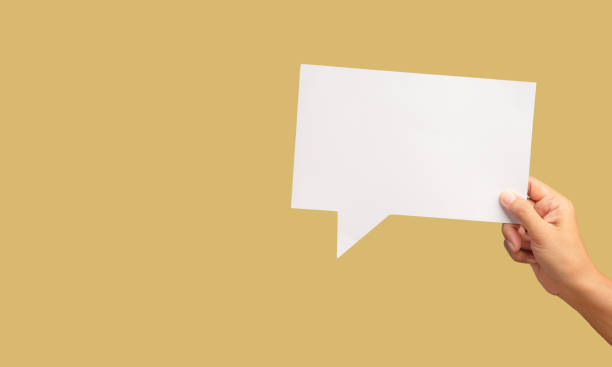 istock Hand holding a blank white speech bubble against a light tannish yellow background. 1928903124
