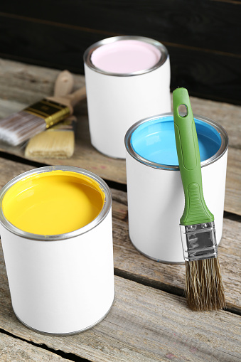 Cans of colorful paints with brushes on wooden table