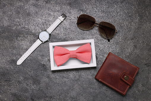 Stylish coral bow tie, sunglasses, wallet and wristwatch on grey textured background, flat lay