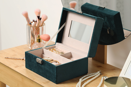 Jewelry box with many different accessories, perfume and makeup brushes on wooden table