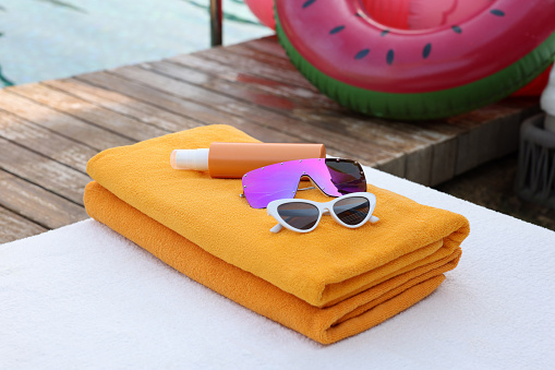 Beach towels, sunglasses and sunscreen on sunbed near outdoor swimming pool. Luxury resort