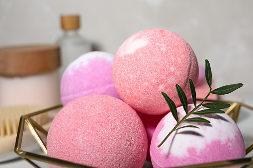 Beautiful aromatic bath bombs and green twig in decorative bowl on blurred background, closeup