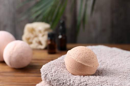Beautiful aromatic bath bomb and towel on wooden table, closeup. Space for text