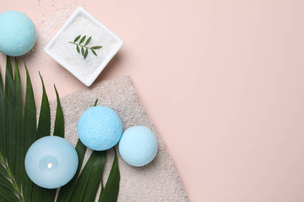 Bath bombs, green leaf, sea salt and burning candle on beige background, flat lay. Space for text