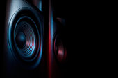 Modern sound speakers in neon light on black background, closeup. Space for text
