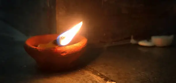 Photo of Indian Festival Diwali, Navratri, celebrations denoted by one glowing lighted Diya Lamp pious flame placed on a concrete floor at the corner of a wall horizontal photograph