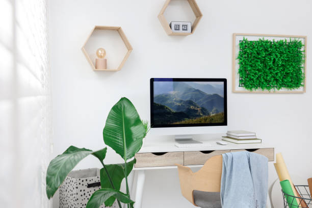 istock Green artificial plant wall panel and desk with computer in light room. Interior design 1929069042