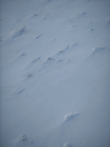 Abstract rough snow ground texture natural snowfield terrain blizzard pattern background. Fresh snow beginning to metamorphose: The surface shows wind packing and sastrugi. In the foreground are hoar frost crystals, formed by refrozen water vapor emerging to the cold surface.
