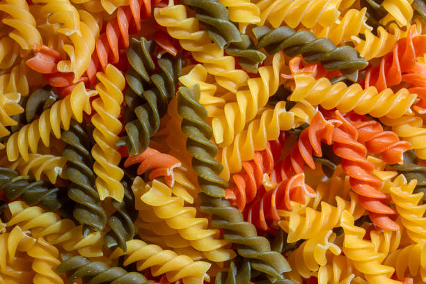 Uncooked Vibrant Colored Fusilli Pasta: A Mesmerizing Culinary Canvas of Multicolored Spirals, Creating a Lively and Textured Background for Gourmet Cooking. Colored Dry Pasta. Raw Macaroni