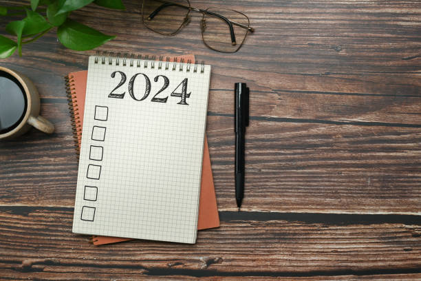 istock 2024 resolutions list in a spiral notebook on wooden table with pen and coffee cup. Creative flat lay 1929323373