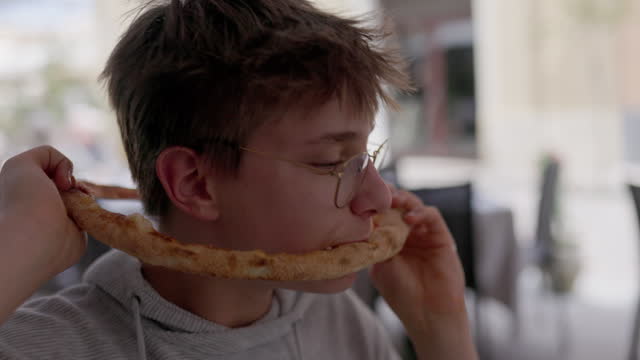 Teenage boy eating pizza in an unusual, funny way
