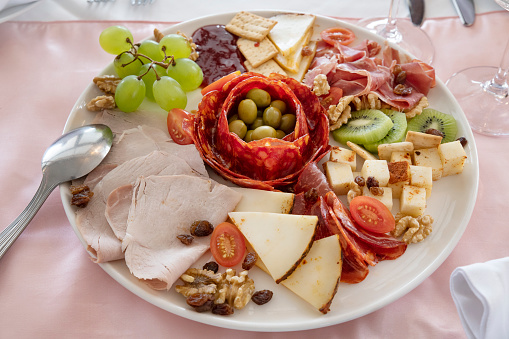 Platter showcasing a diverse array of Spanish cold cuts and cheeses such as chorizos, Serrano and cured hams, along with Manchego and goat cheese, served with crisp crackers, fruit, nuts and olives.