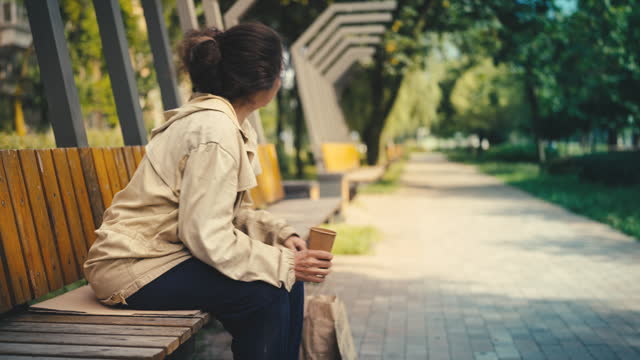Old homeless woman holding paper cup while begging on bench, social inequality
