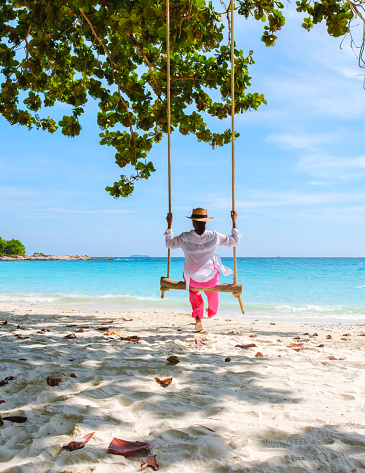 Asian woman on a swing at the beach of Koh Samet Island Rayong Thailand, the white tropical beach of Samed Island with a turqouse colored ocean