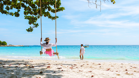 A couple of men and women at a swing on the beach of Koh Samet Island Rayong Thailand, the white tropical beach of Samed Island with a turqouse colored ocean. Asian woman and European men on vacation