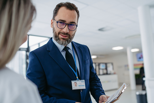 Portrait of pharmaceutical sales representative talking with doctor in medical building. Ambitious male sales representative in suit presenting new medication. Hospital director, manager in private clinic talking with doctor.