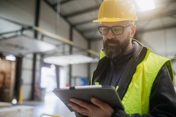 istock Warehouse receiver standing by delivered cargo, holding tablet, looking at cargo details, checking delivered items, goods against order. 1929407562