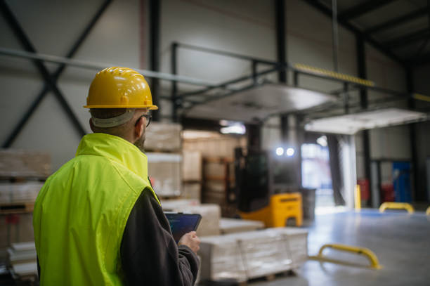 istock Warehouse receiver standing by delivered cargo, holding tablet, looking at cargo details, checking delivered items, goods against order. 1929410593