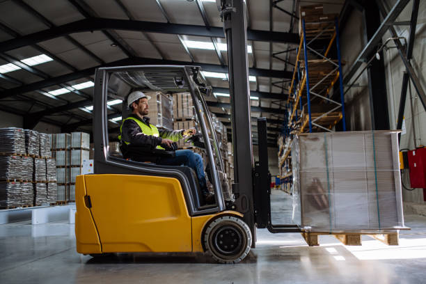 side view of forklift in warehouse with male driver. warehouse worker preparing products for shipmennt, delivery, checking stock in warehouse. - gabelstapler stock-fotos und bilder