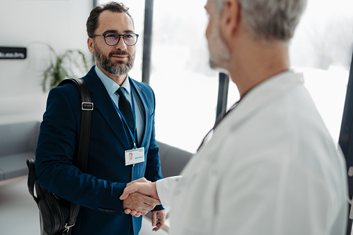 Pharmaceutical sales representative shaking hands with doctor in the medical building. Doctor greeting hospital director, manager in private medical clinic.