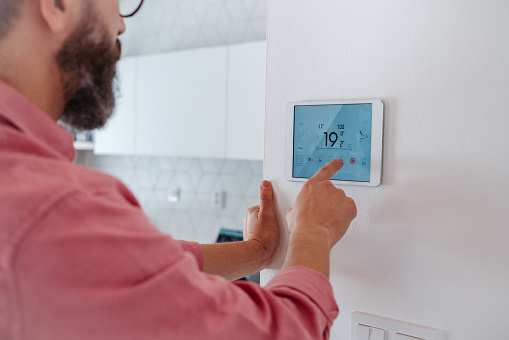Man using smart thermostat, adjusting or lowering heating temperatures at his home. Concept of sustainable, efficient, and smart technology in home heating and thermostats.