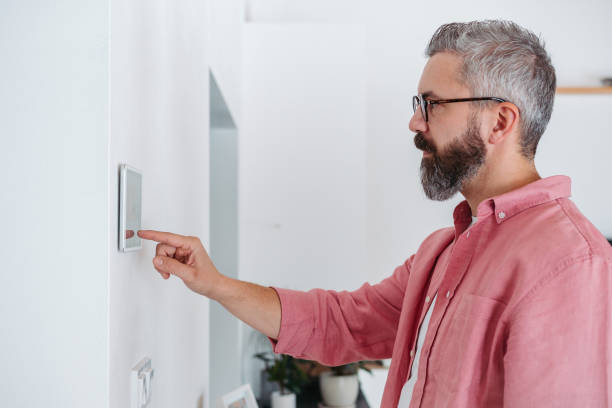 istock Man using smart thermostat, adjusting, lowering heating temperature at home. Concept of sustainable, efficient, and smart technology in home heating and thermostats. 1929431594