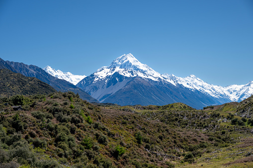 Discover the picturesque landscape in New Zealand's South Island leading to the renowned Mount Cook mountain. Behold the stunning sight of snow-capped Mount Cook, majestically framed by other towering mountain peaks.