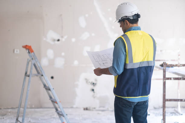 istock Worker in protective hardhat reading project drawing stands near construction safety equipment 1929460356