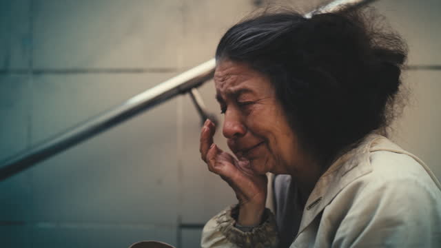 Depressed senior woman crying on stairs with a begging cup, human indifference