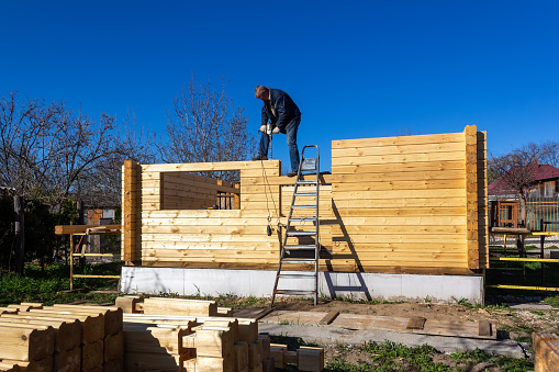 a man builds a house made of profiled timber in the countryside against the blue sky