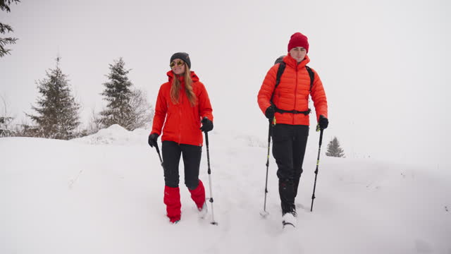 Man and woman hike through mountains and forest on snowy foggy day
