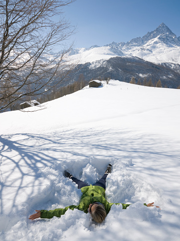 Man makes snow angel in field below mountain