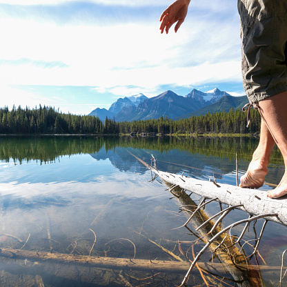 Low angle view of man walking on log over lake towards mountains