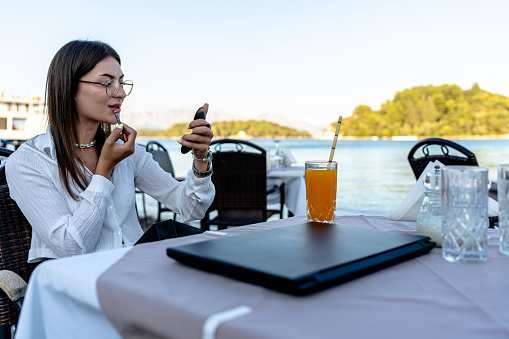 Seated amidst blooming flowers and soft murmurs, the young woman meticulously applies her makeup, embracing the outdoor setting to get the perfect look