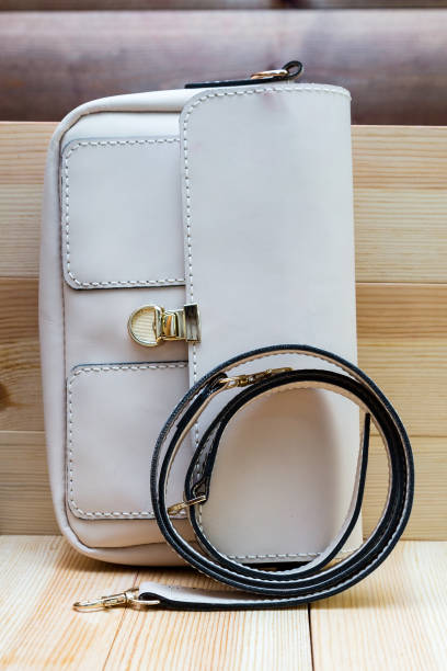 istock White leather women's handbag with a strap on a light wood background. An elegant accessory for stylish women. Handbag made of genuine leather, comfortable and practical. 1929524347