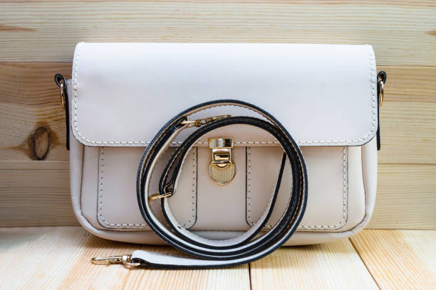 istock White leather women's handbag with a strap on a light wood background. An elegant accessory for stylish women. Handbag made of genuine leather, comfortable and practical. 1929524865