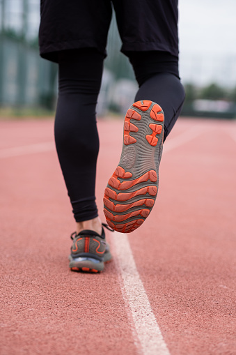 Focused jogger legs in comfortable sneakers races along the red rubberized track at an urban stadium, pushing their limits.