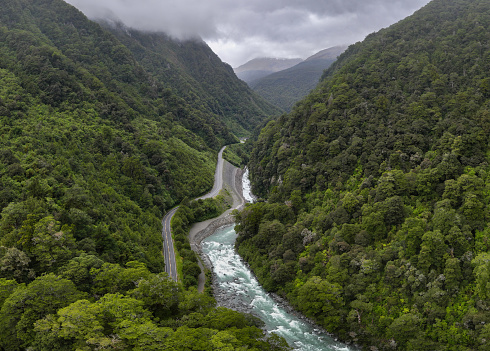 Discover the picturesque country road in New Zealand's South Island leading through lush green rainforest. This view can be seen the city of Haast and Queenstown.