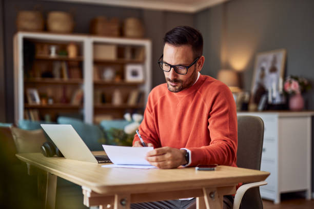 istock Businessman working from home in an orange sweater. He is signing some documents. 1929571479
