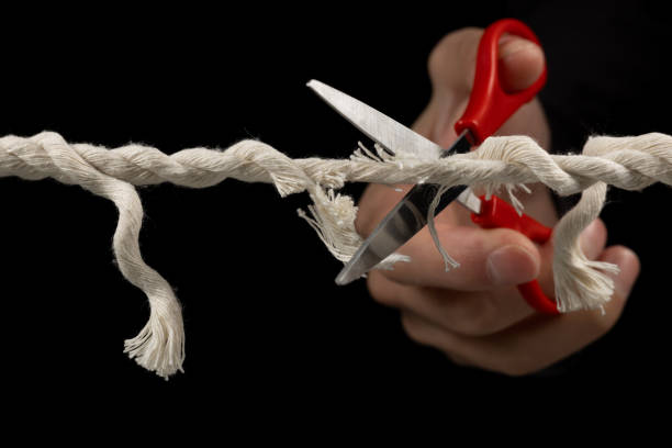 istock Worn rope ready to break, with scissors on black background. 1929573607