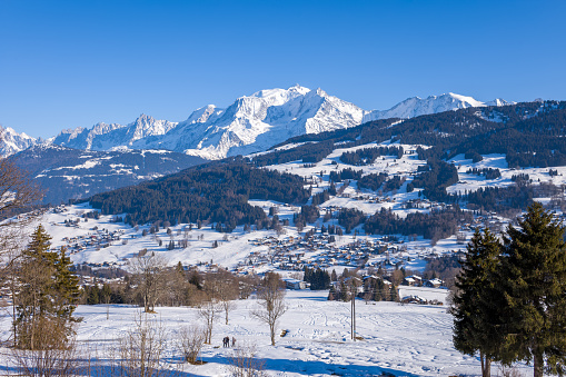 This landscape photo was taken in Europe, in France, Rhone Alpes, in Savoie, in the Alps, in winter. We see the city of Megeve in the middle of the Mont Blanc massif, under the sun.