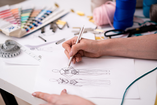 Woman tailor draws glamorous dress sketch with pencil at desk working in fashion atelier dressmaker creates new elements for outfit ornament in shop closeup