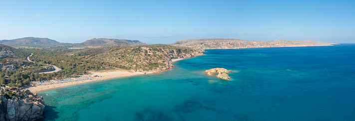 This landscape photo was taken, in Europe, in Greece, in Crete, towards Sitia, At the edge of the Mediterranean Sea, in summer. We see the panoramic view of the arid rocky coast and the fine sandy beach of Vai, under the sun.