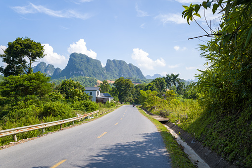 This landscape photo was taken, in Asia, in Vietnam, in Tonkin, towards Hanoi, in Mai Chau, in summer. We see an asphalt road in the middle of the countryside and the mountains, under the Sun.