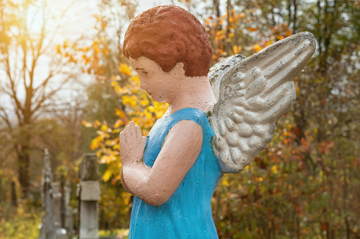 Old statue of an angelic boy in prayer (concept: infant death)